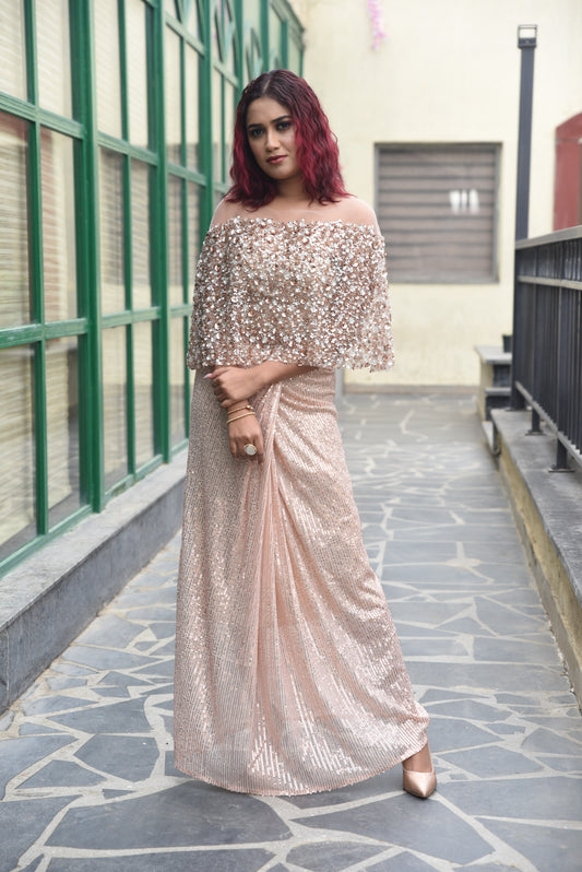 THE OUTFIT FEATURES A ROSE GOLD SEQUIN DRAPE SKIRT PAIRED WITH A MATCHING EMBELLISHED CAPE-STYLE TOP